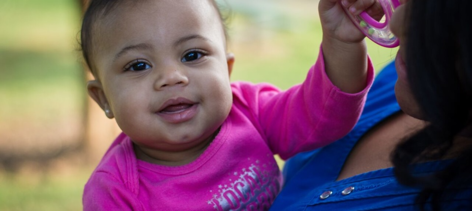 A baby in pink shirt sitting on top of a blue bag.