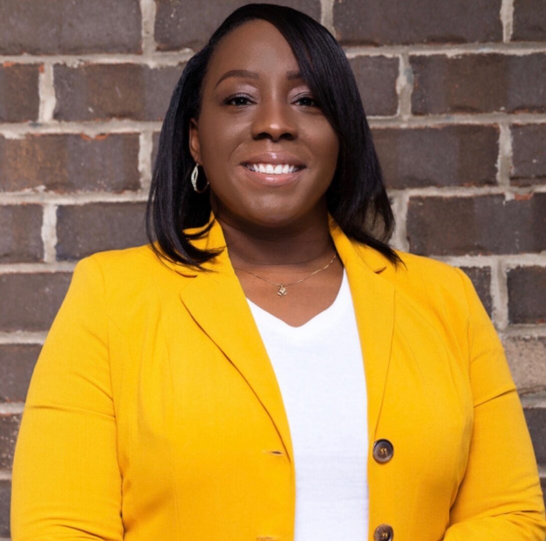 A woman in a yellow jacket standing next to a brick wall.