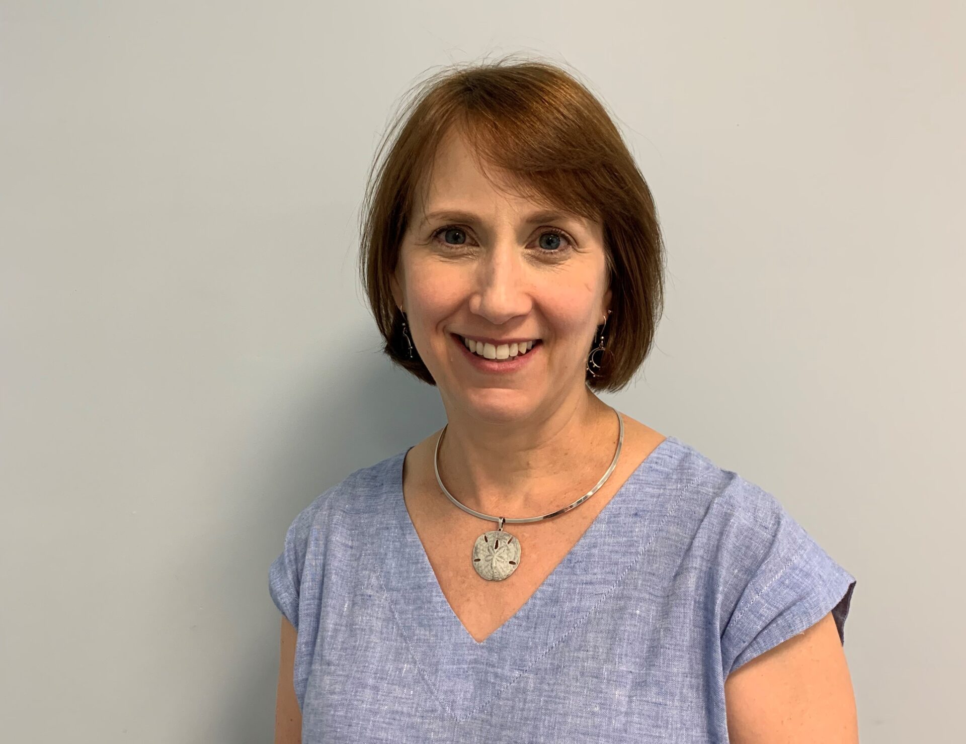 A woman standing in front of a wall smiling.