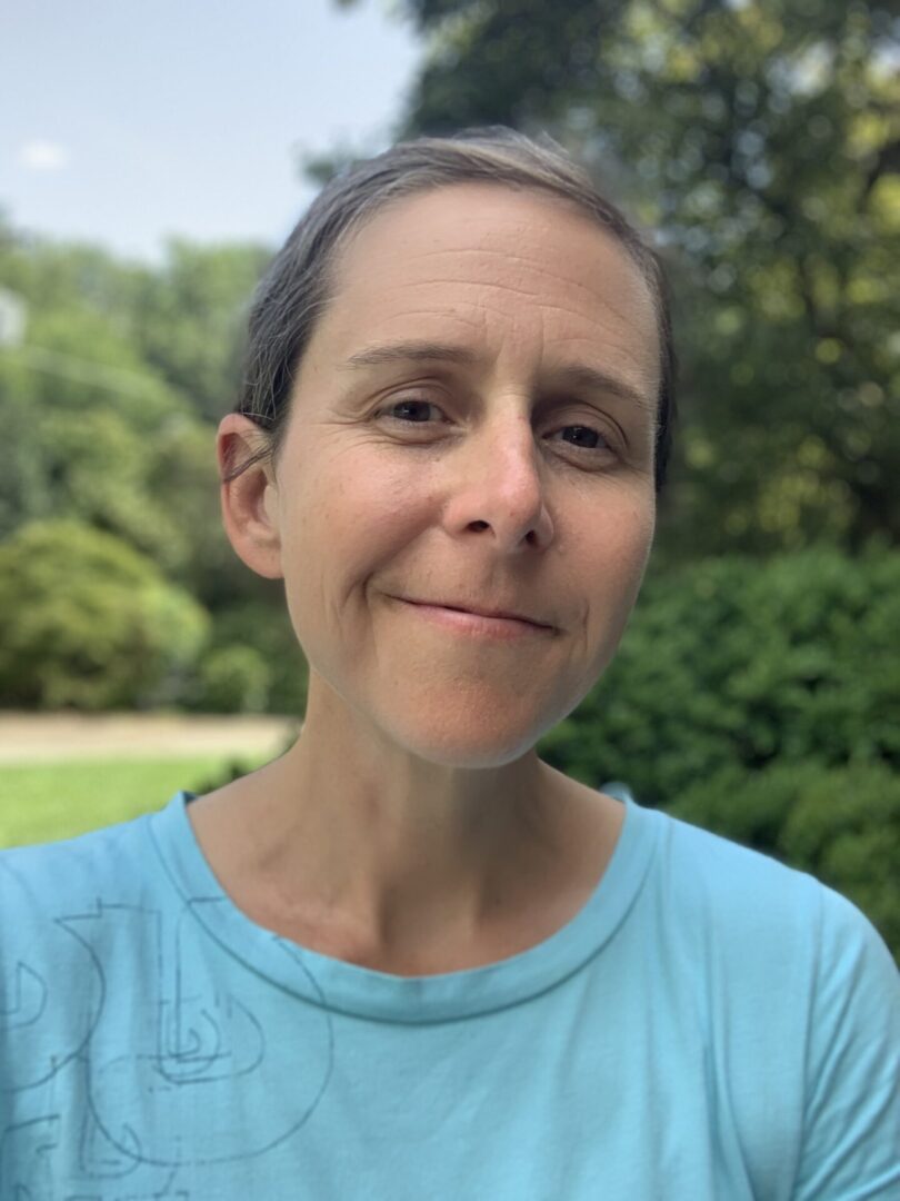 A woman in blue shirt standing next to trees.